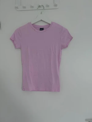Ljusrosa basic t-shirt - En enkel och stilren ljusrosa t-shirt med rund hals och korta ärmar. Perfekt att matcha med jeans eller kjol för en avslappnad look. Tillverkad i mjukt material som känns skönt mot huden.
