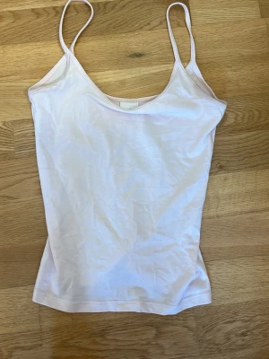 Ljusrosa linnetopp från Gina Tricot - Säljer en enkel och stilren ljusrosa linnetopp från Gina Tricot med tunna axelband. Perfekt att matcha med jeans eller kjol för en clean look. Tillverkad i mjuk bomull som känns skön mot huden.