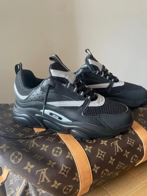 Svarta sneakers - Säljer ett par svarta sneakers med chunky sula och meshdetaljer. Skorna har inslag av vitt och grått, samt tydlig logga på sidan. Kombination av läder och mesh ger en sportig och modern vibe. Perfekta för dig som gillar statement sneakers.