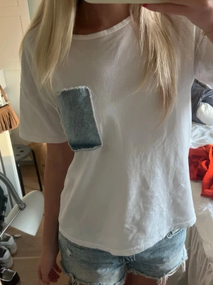 Vit t shirt  - Vit t shirt me en blå denim ficka. Storlek M 
