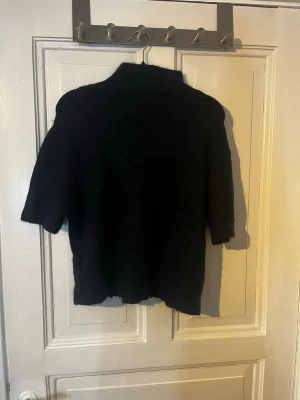 Svart stickad tröja Gina Tricot - Mysig svart stickad tröja från Gina Tricot i ullblandning. Tröjan har halvpolo och kortare ärmar, perfekt för lager på lager. Enkel och stilren design som passar till det mesta.