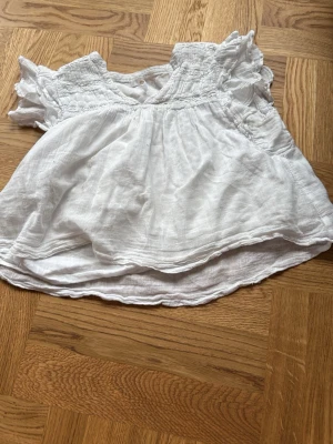 Vit kortärmad blus från Gina Tricot - Söt vit blus från Gina Tricot i ett luftigt och lätt tyg, perfekt för sommaren. Blusen har korta volangärmar, smock upptill och en lös, flowy passform. Materialet ser ut att vara bomull eller linne för en skön känsla.