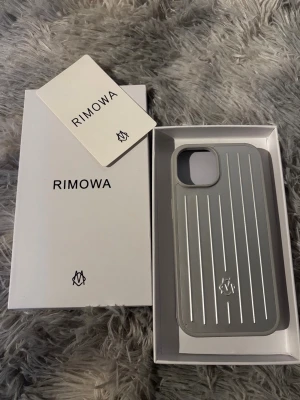 Silverfärgat mobilskal från Rimowa - Nypris 1399kr,Vad jag vet så passar den iPhone 14 och 15. Har inte testat på fler modeller än de!Snyggt och stilrent mobilskal från Rimowa i silverfärgad hårdplast med klassiska räfflade linjer. Skalet har en modern design och skyddar mobilen samtidigt som det ger en exklusiv känsla. Perfekt för dig som gillar minimalistisk och lyxig stil.