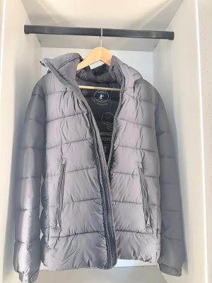 Grå dunjacka från Save The Duck - Snygg grå dunjacka från Save The Duck med quiltat mönster och två dragkedjefickor framtill. Jackan är 100% animal free och tillverkad av återvunnet material. Perfekt för kalla vinterdagar och har en hög krage för extra värme.