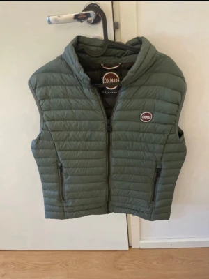 Grön dunväst från Colmar - Snygg grön dunväst från Colmar med quiltad design och dragkedja framtill. Västen har två fickor med dragkedja och en liten Colmar-logga på bröstet. Perfekt för lager-på-lager och håller dig varm under kyliga dagar. 