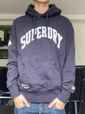 Superdry hoodie - En stilren och snygg marinblå hoodie från superdry i storlek L, sitter som M. Han på bilden är 179. Mycket bra skick. Har du några frågor? Fråga på