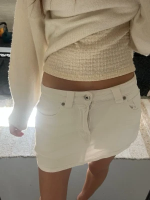Vit kort jeanskjol med fickor - Snygg vit kortkjol i jeansmaterial med klassiska fickor fram och bak, bälteshällor och knappstängning. Perfekt till sommaren och enkel att matcha med olika toppar för en fräsch look.