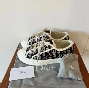 Dior Oblique låga sneakers - Säljer ett par Dior Oblique sneakers i lågt snitt med klassiskt blått och vitt monogrammönster. Skorna har vita snören, gummisula och detaljer i canvas. Perfekta för dig som vill ha en lyxig och trendig look.