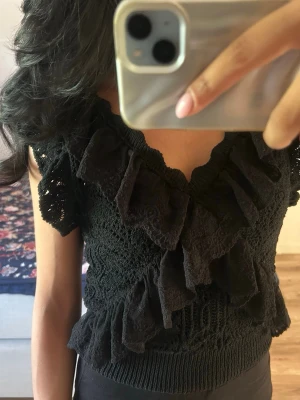 Zara topp - Supersöt svart virkad topp med volanger och v-ringning. Toppen är ärmlös och har en tight passform som framhäver figuren. Perfekt att styla med jeans eller kjol för en trendig look.