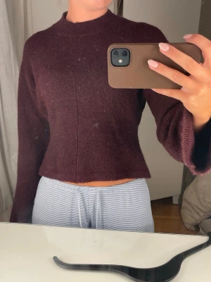 Vinröd stickad tröja med vida ärmar - Mysig vinröd stickad tröja med vida ärmar och rak passform. Tröjan har en högre rund halsringning och är något croppad i modellen.