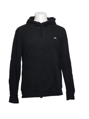 J.Lindeberg Svart hoodie  - Snygg svart hoodie med huva och dragsko samt en liten vit logga på bröstet. Hoodien har en klassisk känguruficka framtill och ribbade muddar vid ärmslut och nederkant. Perfekt för en avslappnad och stilren look.