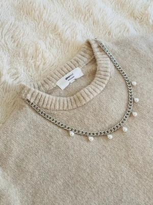 Silverfärgat halsband med pärlor - Snyggt halsband i silverfärgad rostfritt med kedjedesign och hängande vita pärlor. Perfekt för att ge din outfit en trendig touch. Halsbandet har en enkel men cool look och passar till många olika stilar.