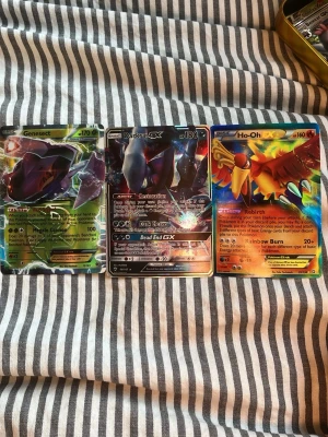 Pokémonkort Genesect, Darkrai GX, Ho-Oh EX - Tre Pokémonkort: Genesect (grön bakgrund), Darkrai GX (svart/lila holografisk) och Ho-Oh EX (färgglad, röd/orange). Alla korten har holografiska effekter och är samlarkort från Pokémon TCG. Perfekt för dig som gillar att samla eller spela Pokémonkort.