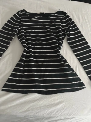 Svartvit randig långärmad topp - Snygg långärmad topp med svart botten och vita horisontella ränder. Figurnära passform med lätt utsvängd nederdel. Perfekt till jeans eller kjol för en stilren look.