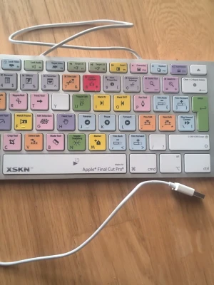 Färgglad Final Cut Pro-tangentbord - Säljer ett specialtangentbord från XSKN för Apple Final Cut Pro. Tangenterna är färgkodade med symboler och genvägar för videoredigering. Tangentbordet har USB-anslutning och är i plast med vit bas och flera färger på tangenterna.