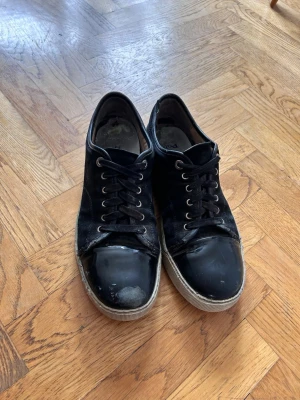 Lanvin cape toe - Snygga svarta sneakers från Lanvin med klassisk låg profil och vita sulor. Skorna har svarta skosnören, metallfärgade öljetter och ovandel i mocka eller läder. Perfekta för en avslappnad streetstil. Sulan är utbytt och under sulan så är det mycket dåligt sick!