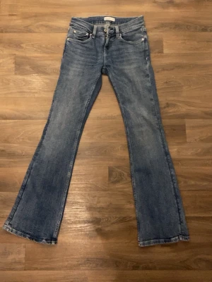 Blå bootcut jeans med utsvängda ben - Säljer ett par klassiska blå bootcut jeans med utsvängda ben och fem fickor. Jeansen har en snygg tvättad look och detaljerade sömmar på bakfickorna. Perfekta för dig som gillar retrostil och vill ha ett par jeans som sticker ut. Jeansen är också lågmidjade. Jeansen har blivit använd en gång innan och att köpa nya kostar 399kr eller 499kr kommer inte ihåg om det var 399 eller 499 jag köpte för. Priser kan diskuteras