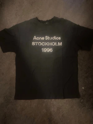 Svart Acne Studios Stockholm 1996 t-shirt  - Säljer en svart t-shirt från Acne Studios med tryck i vitt på bröstet där det står 'Acne Studios STOCKHOLM 1996'. Klassisk passform och rund hals. Perfekt till jeans eller shorts för en clean och enkel look. Kvitto finns
