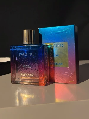 Pacific Aloha parfym 100ml - Snygg parfymflaska från Rayhaan, modell Pacific Aloha. Flaskan är fyrkantig i glas med ett färgskiftande mönster i blått, lila och orange samt guldfärgad kork. Förpackningen matchar flaskans färger och rymmer 100 ml. Perfekt för dig som gillar unika och färgstarka dofter. Använd kanske 3 gånger.