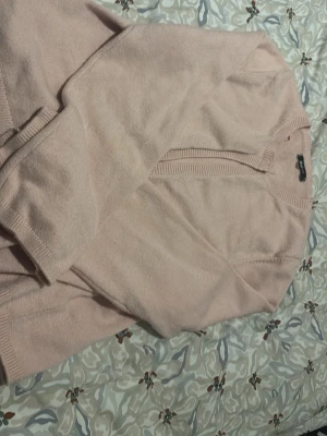 Ljusrosa stickad kofta - Mysig ljusrosa stickad kofta med långa ärmar och ribbade muddar. Koftan har en enkel design med v-ringad halsringning och mjukt material som känns skönt mot huden. Perfekt att slänga över en t-shirt eller topp för en avslappnad look.