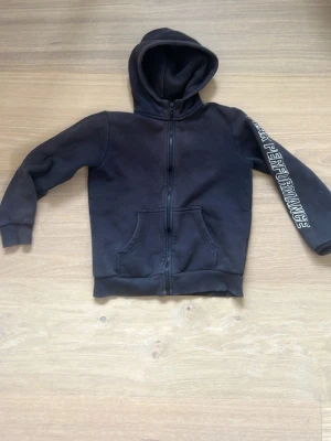 Mörkblå peakperformance hoddie - Säljer en mörkblå hoodie med dragkedja och huva. På ena ärmen står det 'PERFORMANCE' i vitt tryck. Hoodien har två fickor framtill och ribbade muddar vid ärmar och nederkant. 