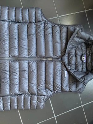 Väst från Patagonia herr - Stilren mörkblå dunväst från Patagonia med quiltad design och hel dragkedja framtill. Dragkedja på fickor. Storlek XL. Fint skick. Ny pris 2300kr