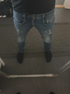 replay 05 aged - Säljer ett par blå jeans med slitningar och trasiga detaljer på låren och knäna. Jeansen har en klassisk femficksmodell och normal passform. Perfekta för en avslappnad och trendig look.