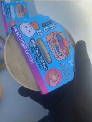 Bun Mystery Squishy Fidget Toy - Rolig squishy-leksak i form av en bun, Sugar Edition. Kommer i en rund förpackning med färgglad etikett. Perfekt för dig som gillar fidget toys och överraskningar, då färgen är en mystery. Passar från 3 år.