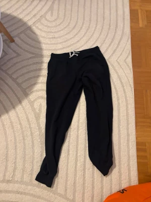 Svarta mjukisbyxor från Pier One - Svarta mjukisbyxor från Pier One med vita dragsnören i midjan. Byxorna har smal passform och muddar vid bensluten. Perfekta för chill eller träning. Tillverkade i mjukt material för maximal komfort.