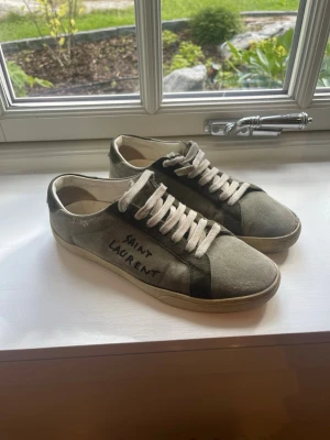 Saint Laurent gröna sneakers - Snygga gröna sneakers från Saint Laurent med handskriven logga på sidan. Skorna har vita snören, beige sula och ovandel i canvas med mockadetaljer. Låg modell som passar perfekt till streetwear och avslappnade outfits.