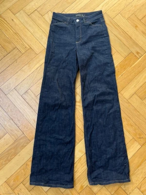 Mörkblå raka jeans från STOCKH LM - Säljer ett par mörkblå (långa!!) jeans från STOCKH LM med hög midja och raka ben. Klassisk femficksmodell med kontrastsömmar och knapp med dekorativ detalj. Jeansen är i ett kraftigt denimtyg och har en tidlös look som passar till många stilar. Använda 1 gång