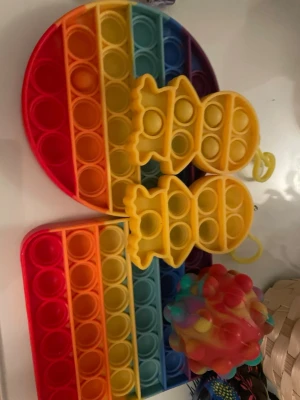 Fidgetleksaker i bland annat regnbågsfärger - Säljer ett set med fidgetleksaker: två pop it-brädor i regnbågsfärger (en rund och en rektangulär), två gula pop it-figurer och en färgglad stressboll med bubblor. Perfekt för dig som gillar att pilla och slappna av.