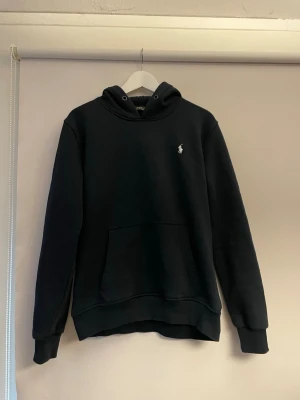 Ralph lauren hoodie - Snygg marinblå hoodie med huva och stor magficka. Klassisk design med en liten vit logga broderad på bröstet. Hoodien har ribbade muddar vid ärmslut och nederkant. Perfekt för en avslappnad och stilren look.