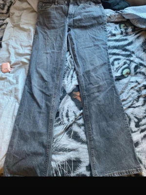 Gråa bootcut jeans - Säljer ett par gråa bootcut jeans med klassisk femficksmodell och hög midja. Jeansen har en lätt tvättad look och raka ben som går ut i en svag utsvängning. Materialet är denim i bomull och de har knapp- och dragkedjestängning.