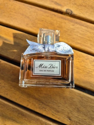 Miss Dior Eau de Parfum 30 ml - Miss Dior Eau de Parfum i en elegant, rektangulär glasflaska med ljusrosa doftvätska. Flaskan har en silverfärgad spray och dekoreras med en glittrig, silverfärgad rosett runt halsen. Perfekt för dig som gillar lyxiga och feminina parfymer. Knappt använd 
