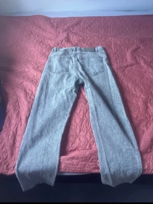 Grå raka jeans från Grunt - Säljer ett par grå jeans från Grunt med rak passform och klassisk femficksdesign. Jeansen har bälteshällor och knappgylf. Materialet är denim i bomull och färgen är ljusgrå med tvättad look. Perfekta för en avslappnad stil.