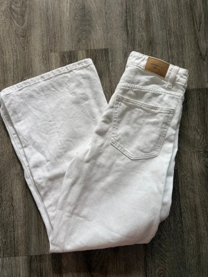 Vita raka jeans med hög midja - Säljer ett par vita jeans med rak passform och hög midja. Jeansen har klassiska fem fickor och bälteshällor. Materialet är kraftigt denim i bomull och de har en stilren look som passar till det mesta. Perfekta för dig som vill ha ett par fräscha och trendiga jeans.