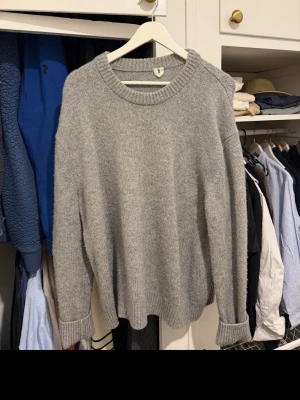 Grå stickad tröja i XL - Klassisk grå stickad tröja med rund hals och ribbade muddar vid ärmslut och nederkant. Perfekt för lager på lager och enkel att matcha med olika outfits. Tröjan har en avslappnad passform och är mjuk och bekväm.
