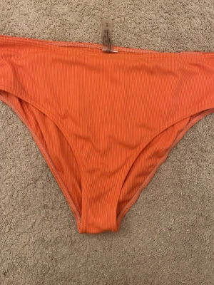 Ribbad orange bikiniunderdel - Snygg bikiniunderdel i en stark orange färg med ribbad struktur. Perfekt för stranddagar och sommarhäng. Klassisk modell med hög benskärning som ger en modern look.