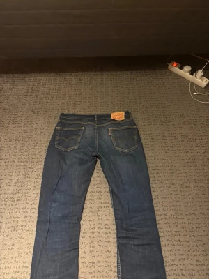 Vintage blå Levis jeans W29, L32 - Säljer ett par blå Levis jeans med raka ben och klassisk femficksdesign. Fin tvätt och snygga detaljer på jeansen. Jeansen har kontrastsömmar och en patch bak i midjan. Materialet är denim och färgen är en djup blå med lätt slitningar. Perfekta till vardagsstilen! Grischstilen. Lappen är lite trasig detta därför att de är vintage 