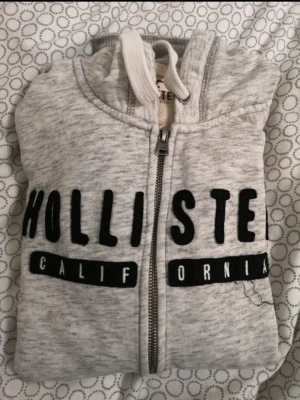 Grå zip hoodie från Hollister - Säljer en kofta från Hollister med borstad insida. Hoodien har fickor framtill och tumhål i muddarna. Står M men skulle säga att den är mindre i storlek, passar mig som är S men jag har ganska breda axlar. Ärmarna är bara lite lång men brukar vika dem