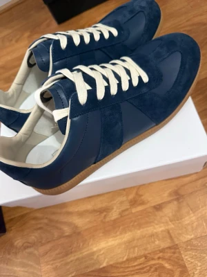 Marinblå sneakers med mockadetaljer - Snygga marinblå sneakers med ovandel i både mocka och slätt läder. Skorna har vita snören och en klassisk gummisula i beige. Insidan är ljus och ger en fräsch kontrast till utsidan. Perfekta för dig som gillar stilrena och tidlösa sneakers.