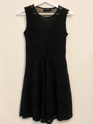 Svart spetsklänning Sisters Point - Supersnygg svart klänning från Sisters Point med spetsdetaljer och geometriskt mönster. Ärmlös modell med rund halsringning och lätt transparent mesh upptill. Perfekt för dig som vill ha en stilren men ändå unik look.