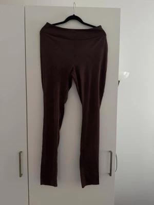 Bruna sammetsleggings med hög midja - Mörkbruna leggings i mjuk sammetsliknande material med hög midja och smal passform. Perfekta för dig som gillar en stilren och bekväm look. Materialet har en lätt glans och känns lyxigt mot huden. Bruna sammetliknande leggings, helt nya och bekväma.