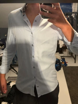Ljusblå skjorta från Stenströms - Säljer en ljusblå skjorta från Stenströms i slim fit med blommigt mönster på insidan av kragen. Skjortan är tillverkad i bomull och har långa ärmar samt knappar framtill. Perfekt för dig som vill ha en stilren men ändå unik look. 15/38 motsvarar S