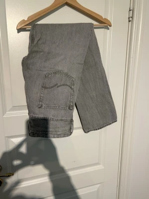 Grå loose fit jeans från Jack and Jones - Säljer ett par grå loose fit jeans med raka ben och stor bakficka. Modellen heter LOOSE/CHRIS och har en avslappnad passform. Perfekta för dig som gillar en chill och trendig stil. Materialet är klassisk denim i bomull.