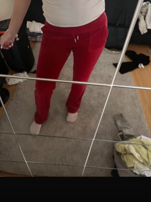 Röda mjukisbyxor i velour - Säljer ett par snygga röda mjukisbyxor i velour med raka ben och dragsko i midjan. Byxorna har fickor bak med lock och knappdetaljer som ger en cool touch. Perfekta för chill dagar eller när du vill vara extra comfy.
