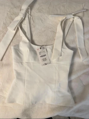 Helt ny zara topp - Supersöt zara topp som aldrig anvants, har rosett detaljer på axelbanden, linne topp, skönt material inuti och har en dragkedja som funkar fint på sidan, den är även lite urringad