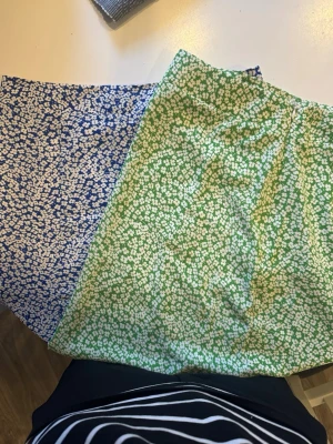 Grön och blå blommig kjol - Säljer en kort kjol med blommigt mönster i grönt och blått med vita små blommor. Kjolen har en A-linjeform och är tillverkad i ett lätt tyg, perfekt för varmare dagar. Supersöt och enkel att matcha med en enkel topp.