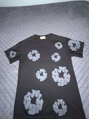 Svart t-shirt med grått mönster - Cool svart t-shirt med unikt grått mönster i form av cirklar över hela tröjan, även på ärmarna. T-shirten har en klassisk passform och är kortärmad. Perfekt för dig som vill sticka ut med en originell stil.